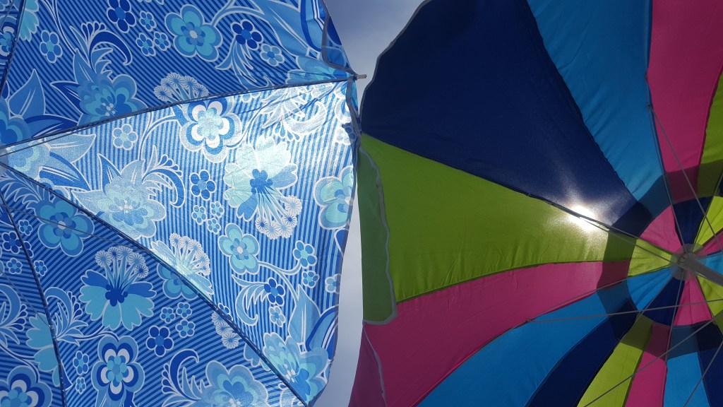 Two umbrellas are shown from underneath. The left one is all blue with blue flowers on it. The right one is stripped with pink, light blue, dark blue, and green.